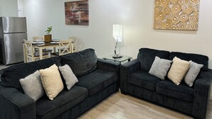 A modern living room with two dark sofas, a dining table, and a refrigerator. - NEW Mcallen Apartament (Pharr)