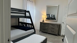 A bunk bed with a dark headboard, a bedside table with a lamp, a dresser with multiple drawers, and a mirror on the wall. - NEW Mcallen Apartament (Pharr)