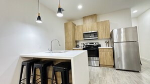 A modern kitchen with a central island, stainless steel appliances, wooden cabinets, and black bar stools. - NEW Mcallen Apartament (Pharr)
