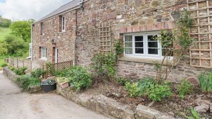 A stone building with a wooden fence, a garden with various plants, and a clear sky. - Corran Cottage (Carmarthen)
