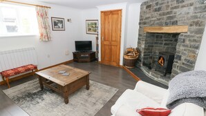 A living room with a fireplace, a sofa, a coffee table, and a television. - Corran Cottage (Carmarthen)