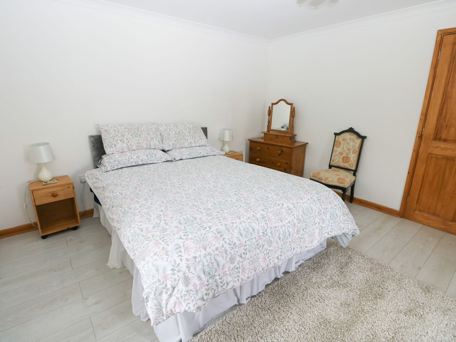 A bedroom with a bed, nightstands, a dresser, a chair, and a wooden door.