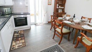 A kitchen with white cabinets, a stove, and an oven. There is a dining table with chairs and a wooden sideboard. - Corran Cottage (Carmarthen)