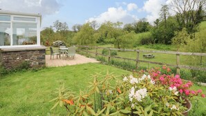 A garden with a stone wall, a wooden fence, and a patio with chairs and a table. - Corran Cottage (Carmarthen)