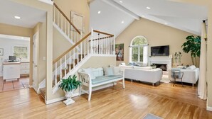 A spacious living room with a wooden staircase, a fireplace, and a television. - Summer in Bridgehampton beautiful home minutes from Bridgehampton and Sag Harbor (Bridgehampton)
