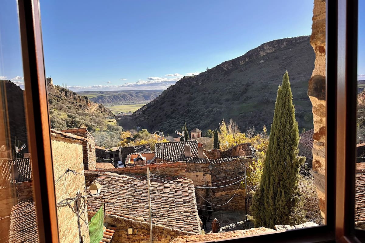 A view from a window overlooking a valley with traditional buildings and a mountain in the background.