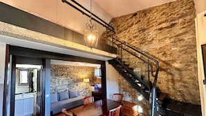 A modern living room with a stone wall, a wooden dining table, and a staircase. - El Bulín de Patones (Patones)