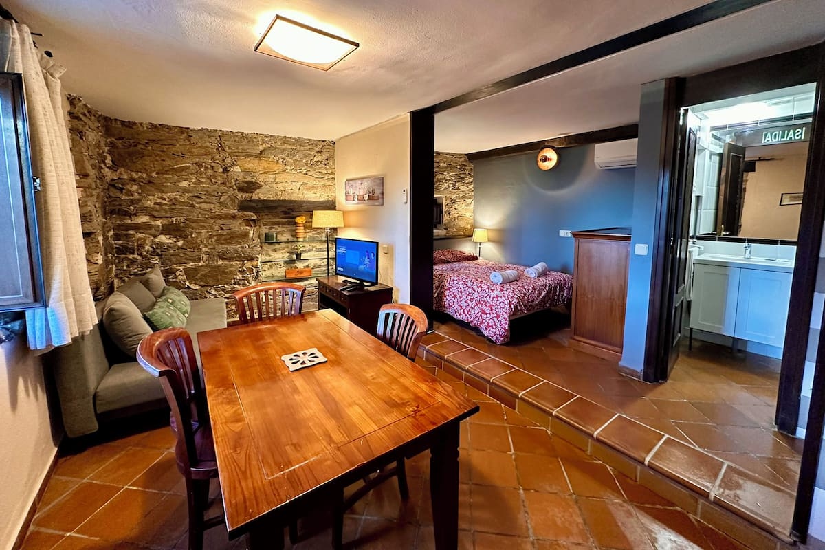 A cozy room with a wooden dining table, a sofa, a TV, and a bed with a floral bedspread.