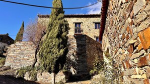 A stone building with a balcony, surrounded by trees and a clear blue sky. - El Bulín de Patones (Patones)