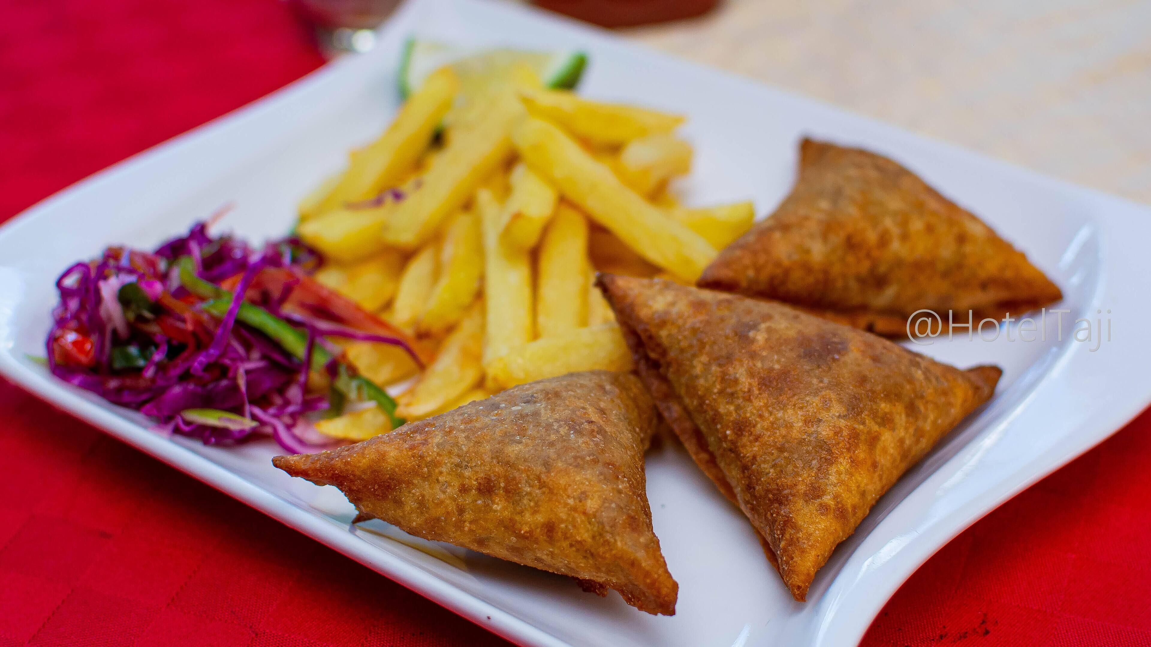 A plate with three samosas, French fries, and a side salad.