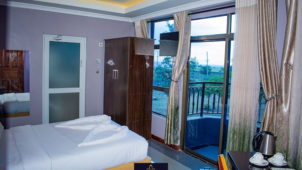 Habitación de hotel con cama, armario, balcón con vistas y una mesa con hervidor y tazas.