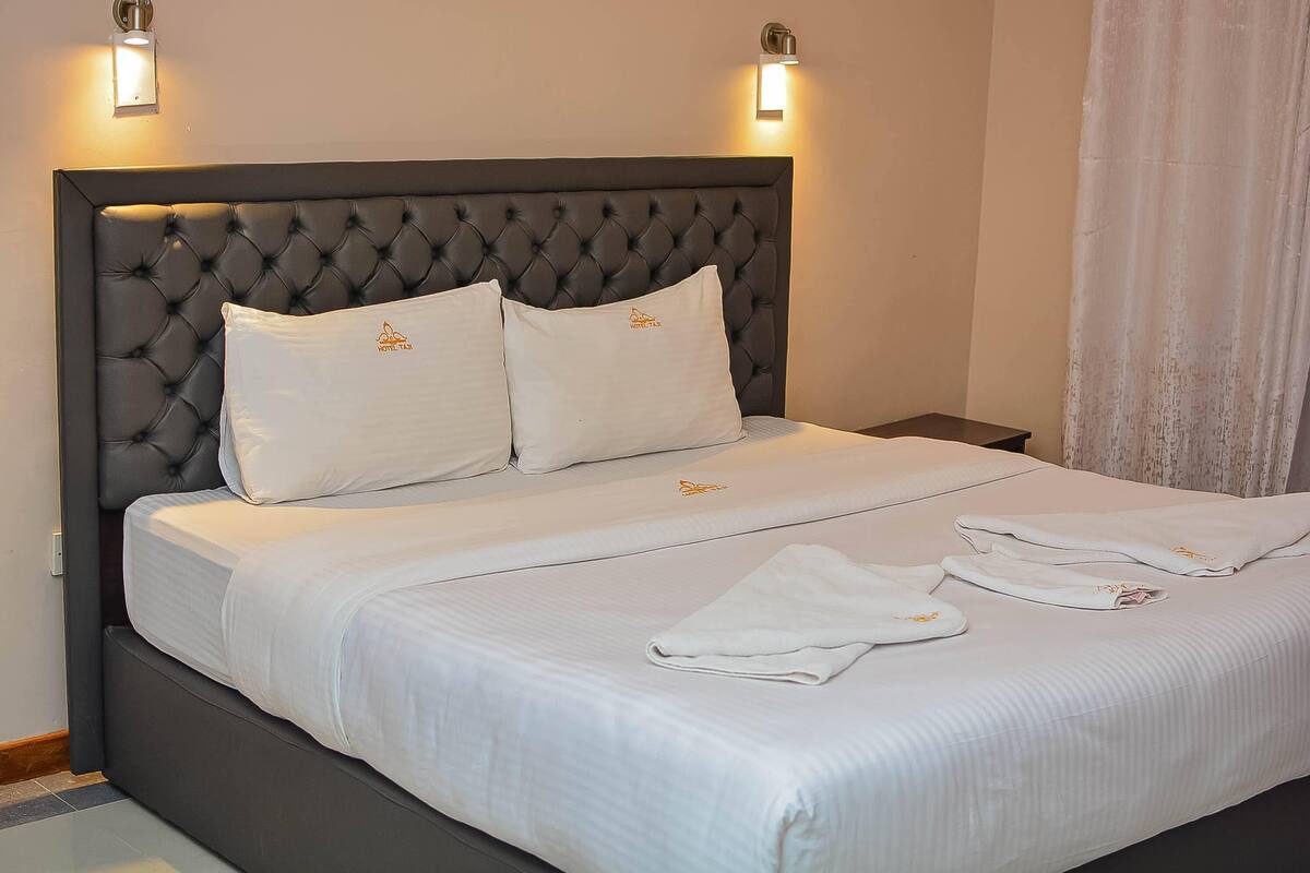 A neatly made bed with white linens and pillows, a tufted headboard, and two wall-mounted light fixtures.