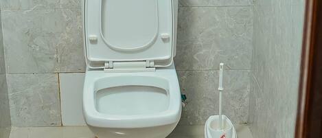 Casa de banho com sanita, suporte para rolo de papel higiénico e desentupidor.