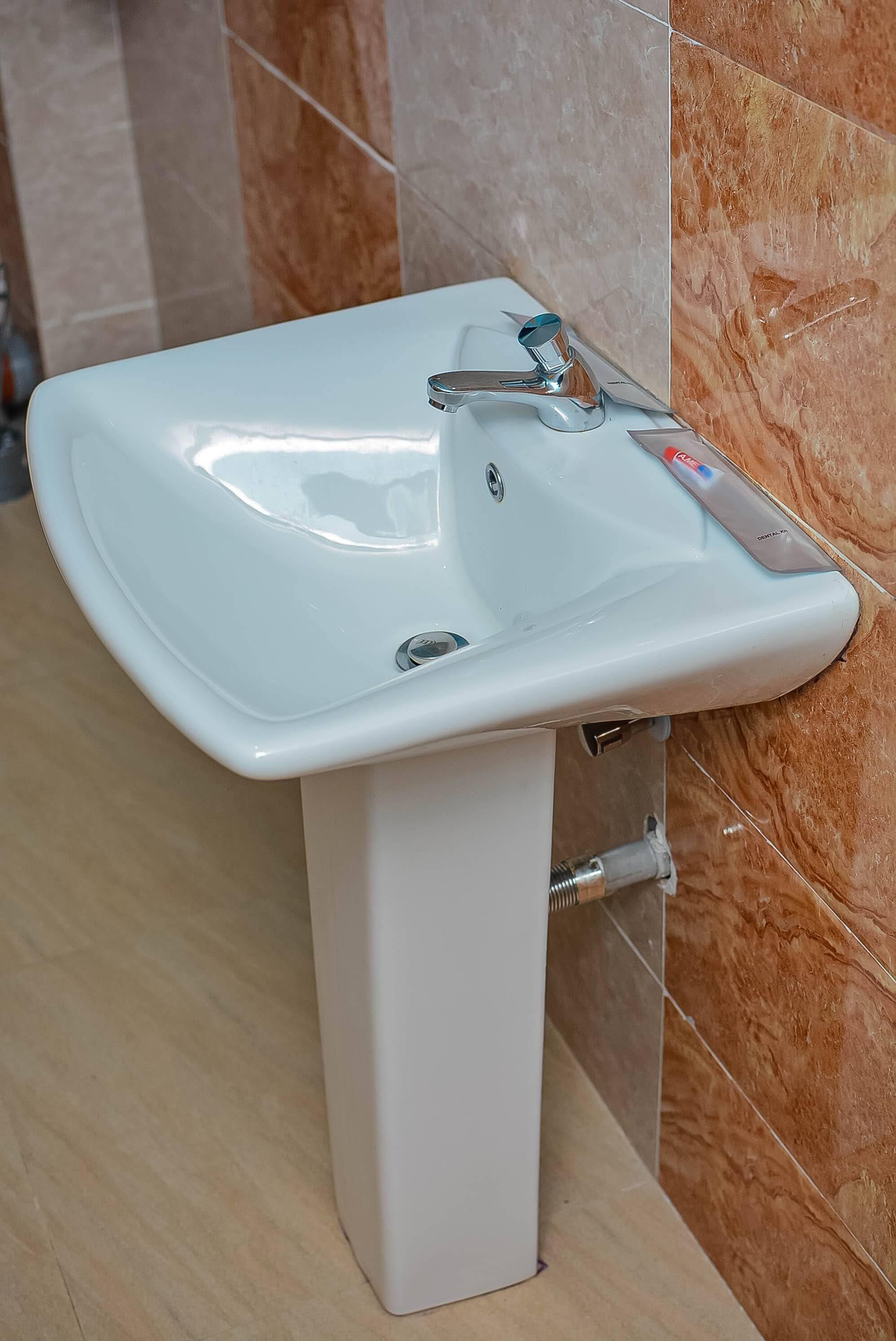 A white pedestal sink with a modern faucet in a bathroom with marble tiles.