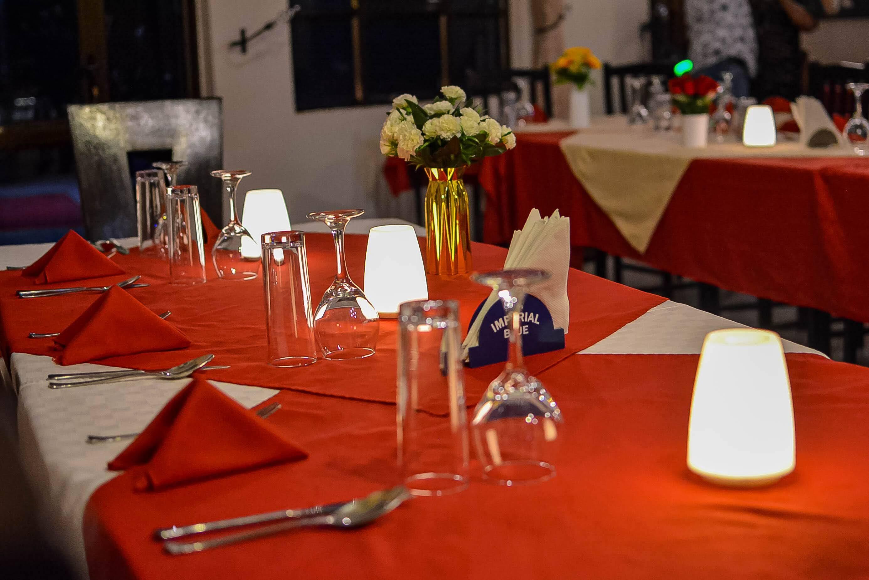 Een eettafel gedekt met rode servetten, glazen en een vaas met witte bloemen.