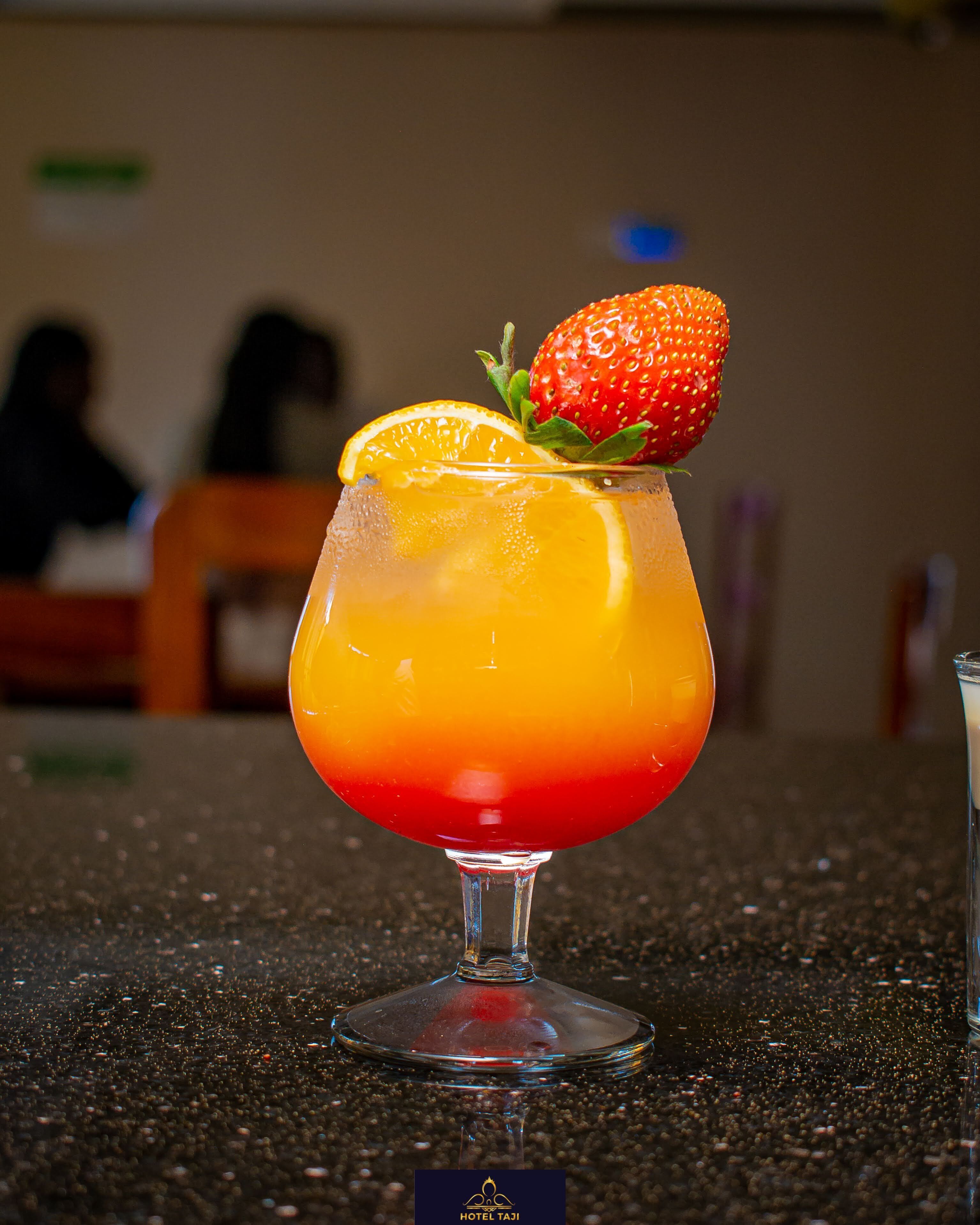 Cóctel con una rodaja de fresa y naranja, servido en una copa con pie.