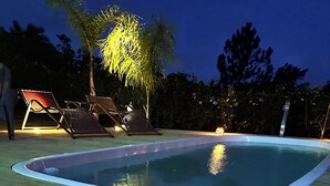 An outdoor swimming pool with a wooden deck, surrounded by palm trees and a chair. - Altos da Lagoa-praia do Rosa, Ibiraquera -studio 3 (Imbituba)