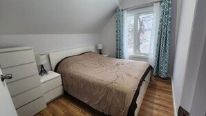 Une chambre à coucher avec un lit, une commode, une table de chevet et une fenêtre avec des rideaux.