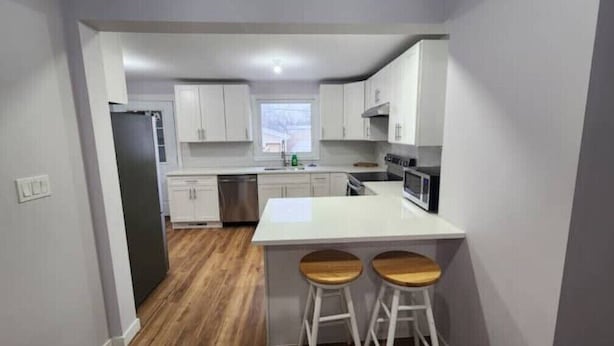 Une cuisine moderne avec des meubles blancs, un îlot central doté de tabourets et une vue sur l’extérieur.