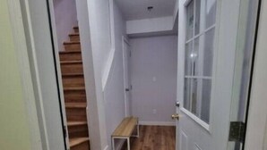 Un couloir étroit avec un plancher en bois, un banc et une porte dotée d’une fenêtre.