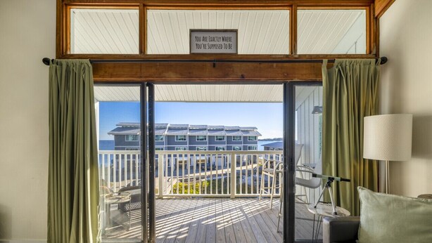 A room with a sliding glass door leading to a balcony with a view of a building. - Top floor condo with sunset Gulf views (Cedar Key)