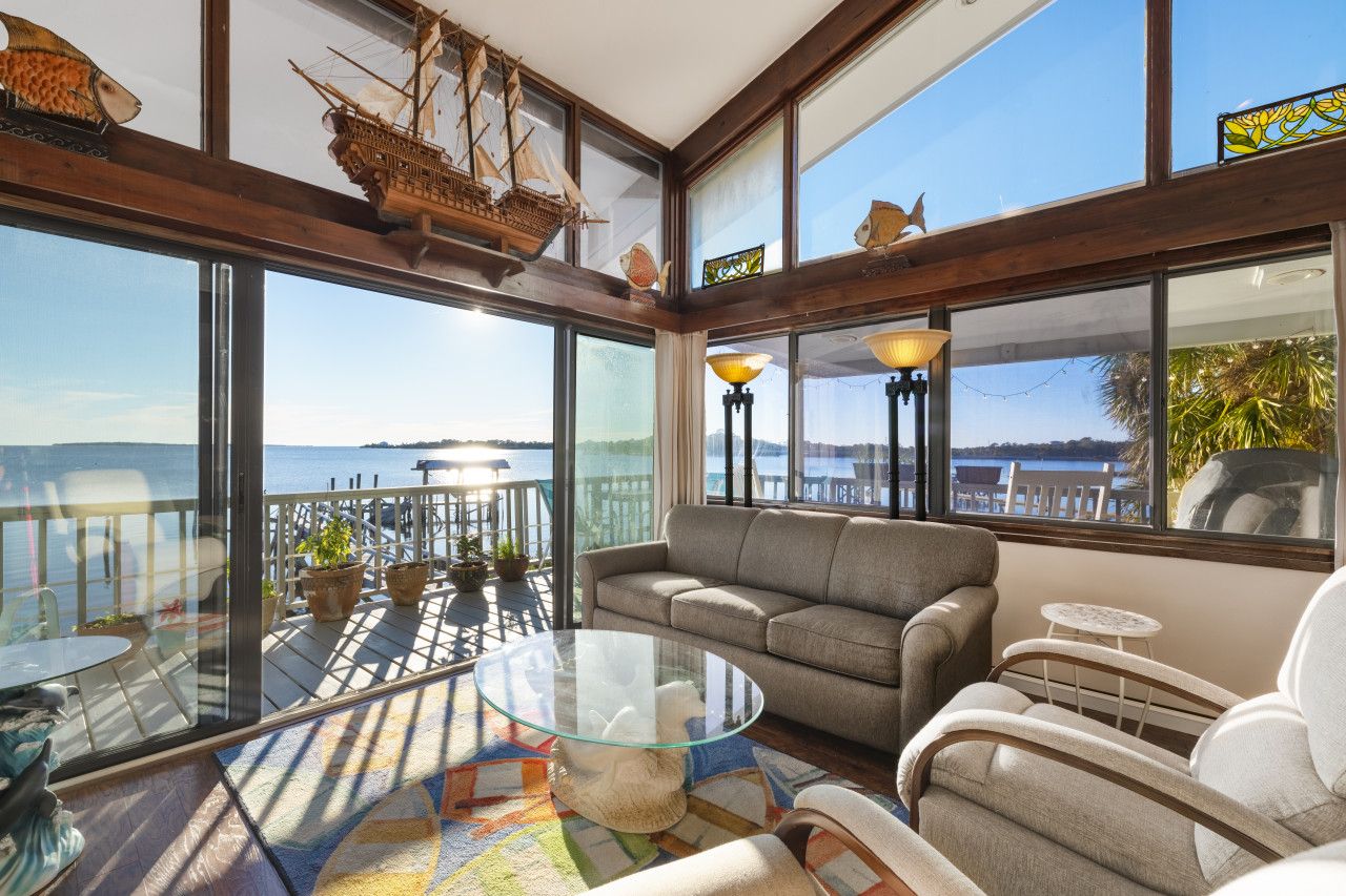 A spacious balcony with a glass table, a sofa, and chairs, overlooking a body of water.