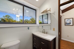 A bathroom with a white toilet, dark wooden vanity, a large window with a view of a water tower, and a framed picture on the wall. - Enjoy the best of Cedar Key with the walkable waterfront (Cedar Key)