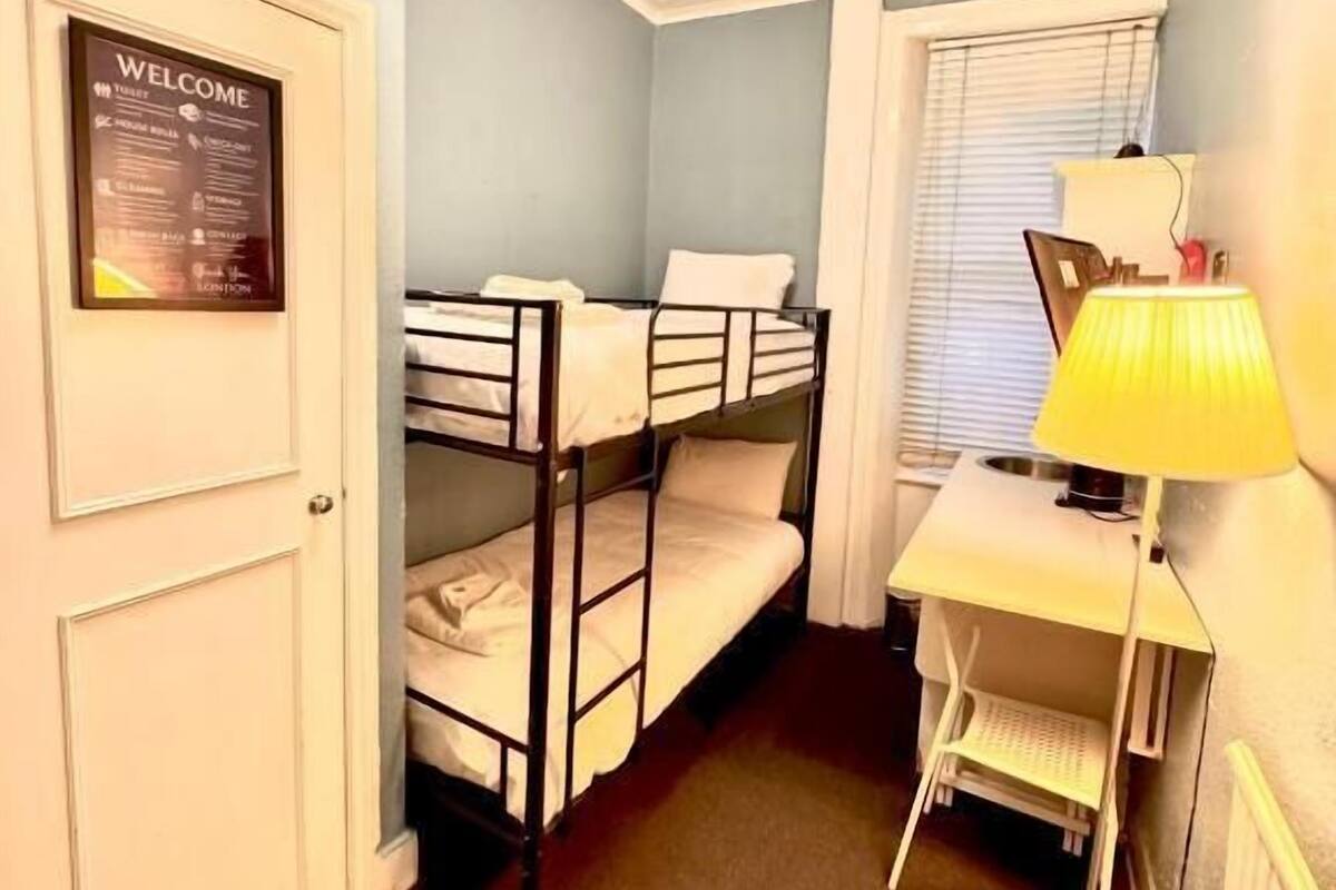 A small, compact room with bunk beds, a desk, and a lamp.