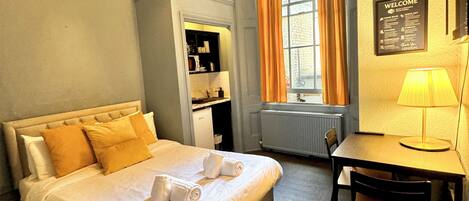 A hotel room with a bed, a desk, a chair, a wardrobe, a window with curtains, and a chandelier.