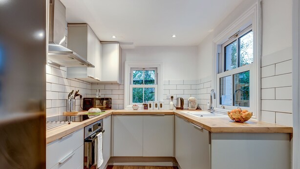 A modern kitchen with white cabinetry, a wooden countertop, a built-in oven, and a window with a view of trees. - Henley Street Townhouse | Oxford Holiday Let | 3 Beds & Sleeps 6 (Oxford)