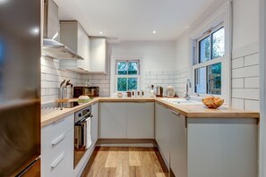 A modern kitchen with white cabinetry, a wooden countertop, a built-in oven, and a window with a view of trees. - Henley Street Townhouse | Oxford Holiday Let | 3 Beds & Sleeps 6 (Oxford)