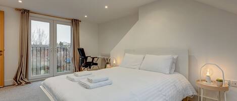 A bedroom with a large bed, a chair, a bedside table with a lamp, and a view through a sliding door to the outside.