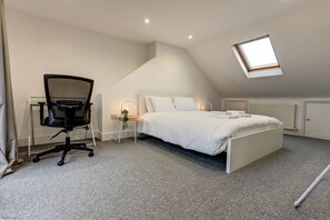 A bedroom with a sloped ceiling, a bed, a desk, and a chair. - Henley Street Townhouse | Oxford Holiday Let | 3 Beds & Sleeps 6 (Oxford)