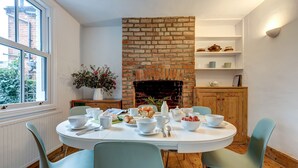 A dining area with a brick fireplace, white walls, and a window overlooking greenery. - Henley Street Townhouse | Oxford Holiday Let | 3 Beds & Sleeps 6 (Oxford)