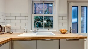 A kitchen with a white sink, wooden countertop, and a window with a view of a brick building and greenery. - Henley Street Townhouse | Oxford Holiday Let | 3 Beds & Sleeps 6 (Oxford)