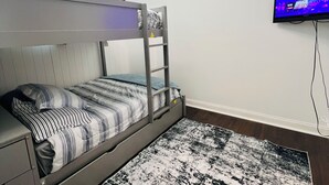 Ein Stockbett mit einer Leiter, einem Flachbildfernseher und einem gemusterten Teppich in einem Zimmer mit weißen Wänden und einer Deckenleuchte.