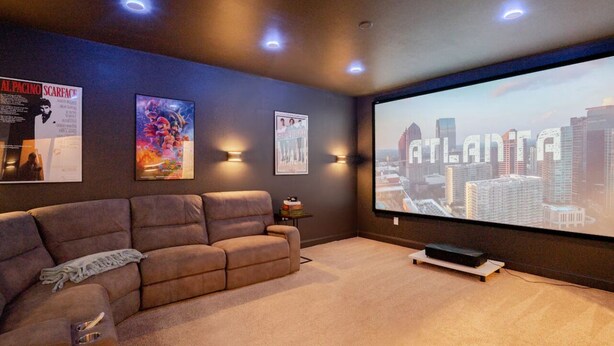 Ein Heimkinozimmer mit einer großen Leinwand, die 'ATLANTA' zeigt, einem braunen Sofa und Postern an der Wand.