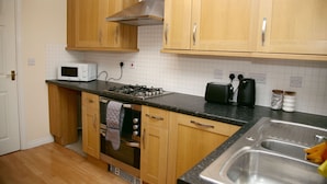 A kitchen with wooden cabinets, a microwave, a stove, and a sink. - 8 Guests - 4 Bedrooms - Parking - Garden (Norwich)