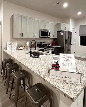 A modern kitchen with granite countertops, stainless steel appliances, and bar stools. - New Built - Clean - Comfort (Grand Junction)
