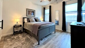 Une chambre à coucher comprenant un lit, une table de chevet, un bureau, un ventilateur de plafond, une fenêtre et une vue sur l’extérieur.