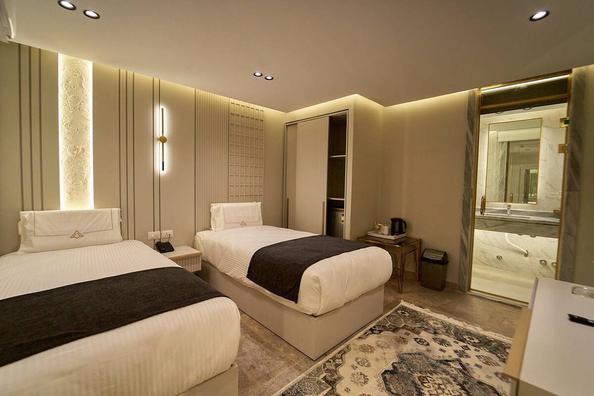 A modern hotel room with two beds, a walk-in closet, a bathroom with a large mirror, and a patterned rug.