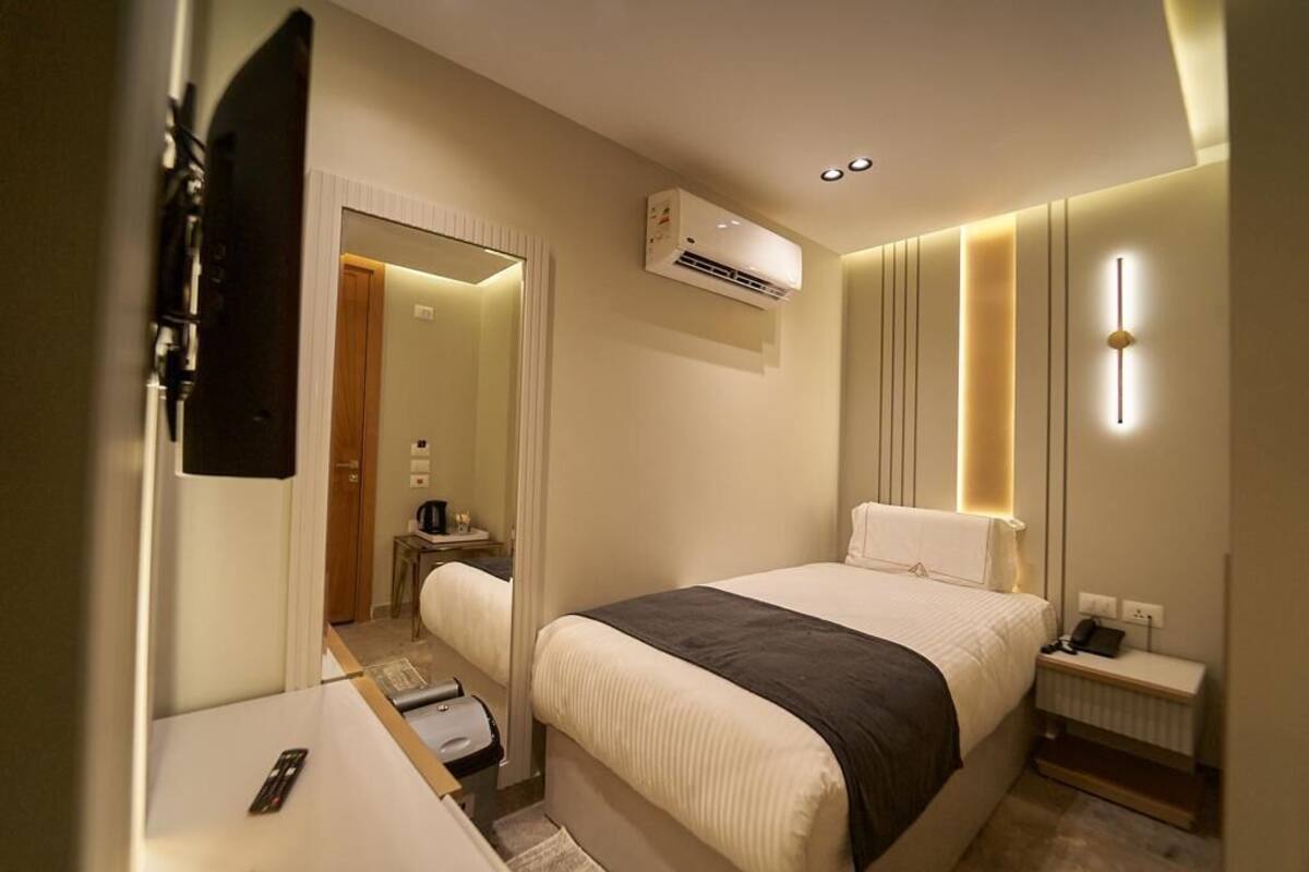 A hotel room with a bed, bedside table, and a mirror.