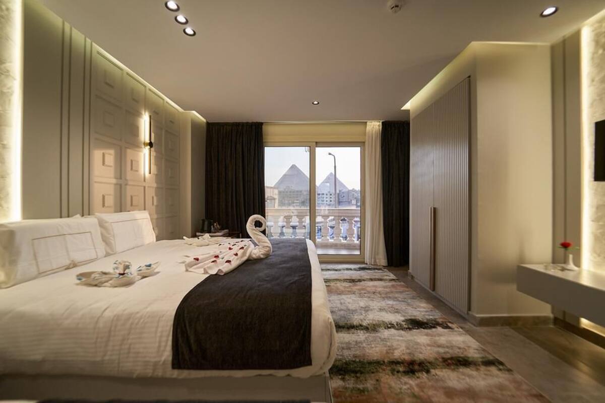 A hotel room with a large bed, a view of a pyramid, and a balcony with a railing.