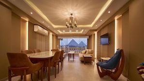 A spacious room with a dining area, a sofa, and a unique curved chair. A chandelier hangs from the ceiling, and a TV is mounted on the wall. - Pyramids Charm (Giza)