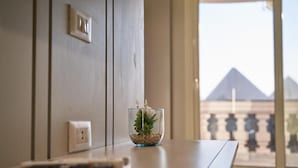 A hotel room with a view of pyramids through a large window, a remote control on the table, and a small glass vase with a plant. - Pyramids Charm (Giza)