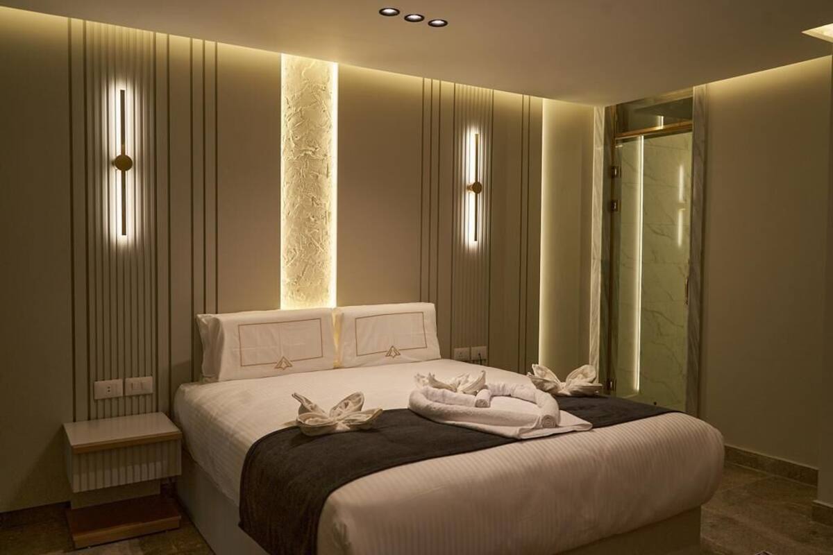 A modern hotel room with a large bed, a built-in wall-mounted light, a shower, and a small bedside table.