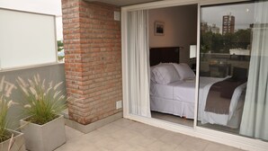 A hotel room with a bed, a sliding glass door, a brick wall, and potted plants. - Livin Residence (Rosario)