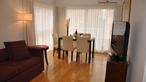 A living room with a sofa, a dining table with chairs, a TV on a stand, and a lamp. - Livin Residence (Rosario)