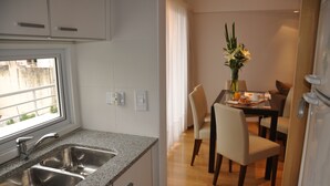 A modern kitchen with a granite countertop, stainless steel sink, and a dining area with a table, chairs, and a vase of flowers. - Livin Residence (Rosario)