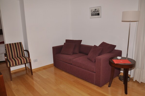 A living room with a red sofa, striped chair, and a small round table with a lamp. - Livin Residence (Rosario)